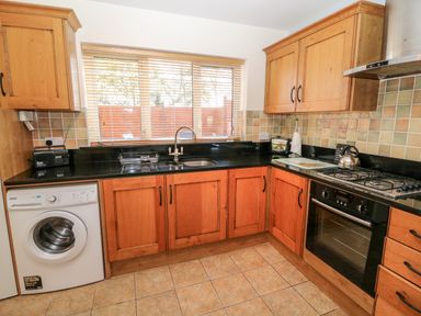 A kitchen with wooden cabinets a washing machine an oven a stove and a sink at The Blue Annex The Spa near Tralee County Kerry