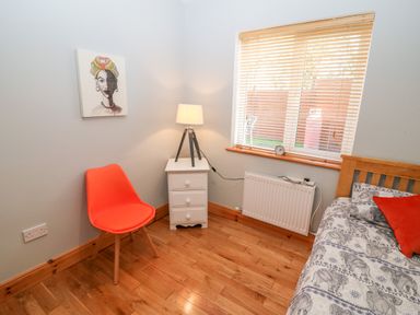 A room with a wooden floor an orange chair a white bedside table with a lamp a window radiator and a bed with elephant patterned bedding and a red pillow at The Blue Annex The Spa near Tralee County Kerry