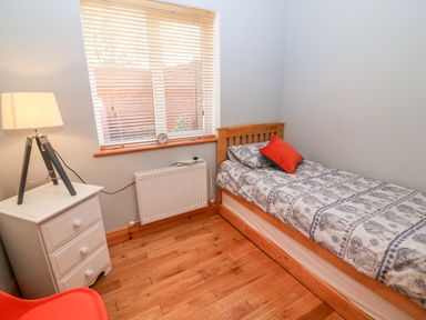 A bedroom with a single wooden bed white bedside table with lamp and window blinds at The Blue Annex The Spa near Tralee County Kerry
