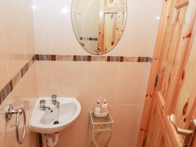 A small bathroom with a corner sink an oval mirror wooden door and a small table with bottles at The Blue Annex The Spa near Tralee County Kerry