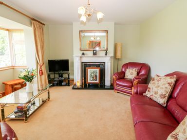 A living room with red leather sofa and armchair near a fireplace and a glass coffee table with flowers at The Blue Annex in The Spa near Tralee County Kerry