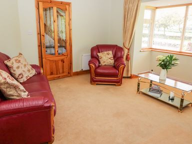 A living room with red leather sofa and armchair beige carpet glass coffee table with flowers at The Blue Annex in The Spa near Tralee County Kerry