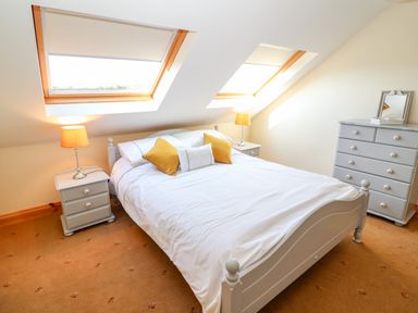 A bedroom with a bed with white bedding and yellow pillows two bedside tables with lamps a grey dresser and skylight windows at The Blue Annex The Spa near Tralee County Kerry