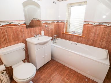 A bathroom with a toilet, sink with cabinet, bathtub, mirror, and window at The Blue Annex The Spa near Tralee County Kerry