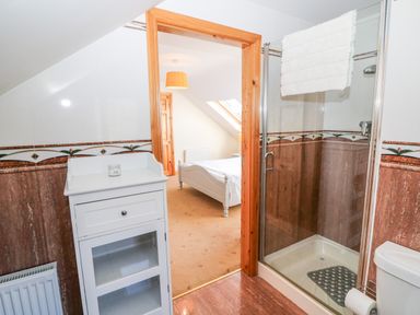 A bathroom with a shower, white cabinet, and toilet visible through a wooden door leading to a bedroom at The Blue Annex in The Spa near Tralee County Kerry