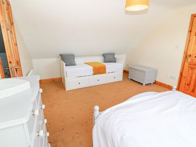 A bedroom with a white daybed with cushions a grey chest of drawers and a white bed at The Blue Annex The Spa near Tralee County Kerry