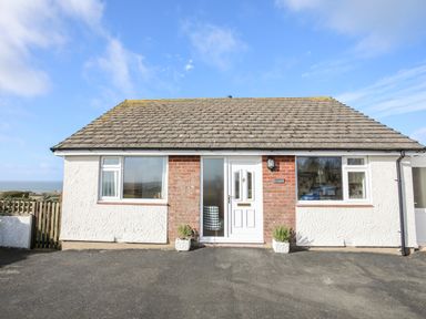 A single story house with white walls and a tiled roof with a paved driveway at Yr Orsedd in Llanfaethlu