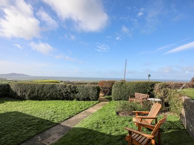 A garden with wooden chairs and a bench overlooking the sea at Yr Orsedd in Llanfaethlu