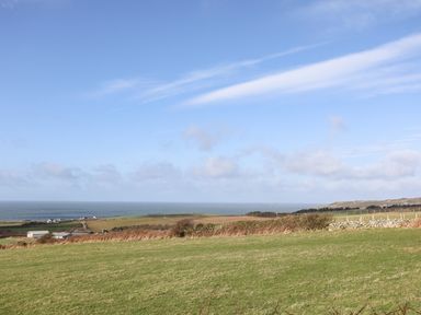 A grassy field with hedges and houses in the distance overlooking the sea at Yr Orsedd in Llanfaethlu