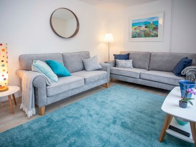 A living room with two grey sofas a blue rug a round mirror and a floor lamp at Bryn Teg Cottage in Menai Bridge