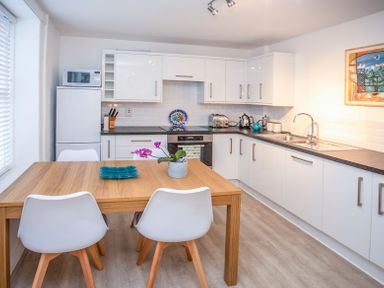 A kitchen with white cabinets wooden table and white chairs at Bryn Teg Cottage in Menai Bridge
