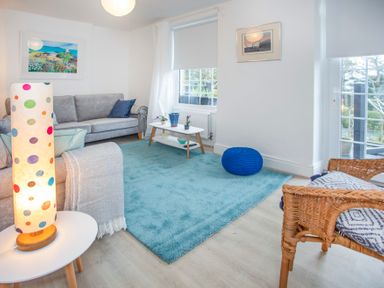 A living room with grey sofa blue rug and wicker chair at Bryn Teg Cottage in Menai Bridge