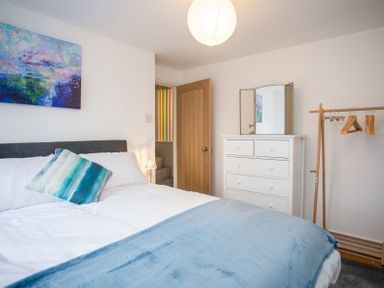 A bedroom with a bed a blue pillow a white dresser with mirror an open wooden door and a wooden clothes rack at Bryn Teg Cottage in Menai Bridge