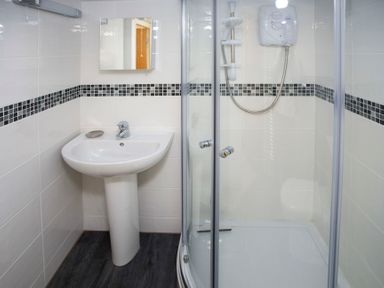 A bathroom with a pedestal sink a wall-mounted mirror and a glass-enclosed shower at Bryn Teg Cottage in Menai Bridge