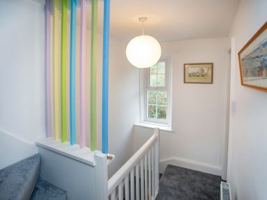 A staircase landing with grey carpet and a window with white frame and a hanging light at Bryn Teg Cottage in Menai Bridge