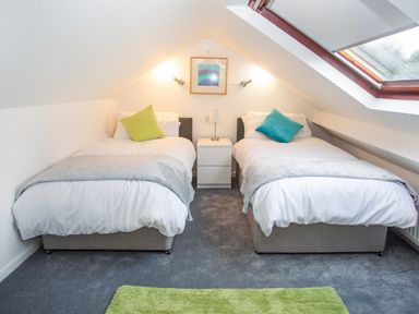 A bedroom with two single beds separated by a bedside table under a slanted ceiling with a skylight at Bryn Teg Cottage in Menai Bridge