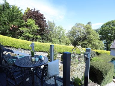 An outdoor patio with a metal table and chairs with cups and a teapot surrounded by trees and bushes at Bryn Teg Cottage in Menai Bridge