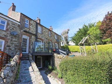 Stone house with balcony and garden area with wooden structure and trimmed hedges at Bryn Teg Cottage in Menai Bridge