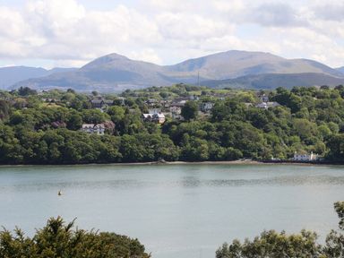 A wide river with houses and trees on the opposite bank and mountains in the background at Bryn Teg Cottage in Menai Bridge