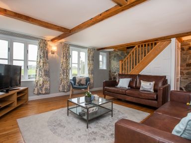 A living room with leather sofas a glass coffee table a blue armchair and a television at Stabl Bach in Llanfaethlu