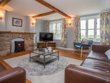 A living room with a stone fireplace television armchair coffee table and floral curtains at Stabl Bach in Llanfaethlu