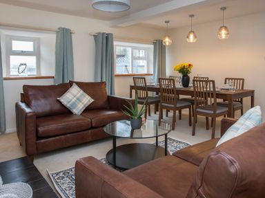 A living room with two brown leather sofas a round glass coffee table and a dining table with chairs at Stabl Bach in Llanfaethlu