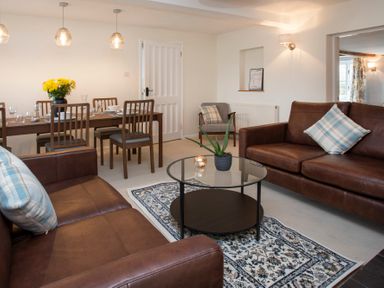 A living room with brown leather sofas a round glass coffee table and a dining table with wooden chairs at Stabl Bach in Llanfaethlu