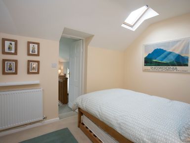 A bedroom with a bed under a skylight and framed pictures on the wall at Stabl Bach in Llanfaethlu