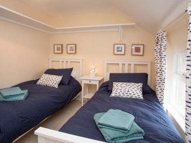 A bedroom with two single beds with blue bedding a white nightstand with a lamp and framed pictures on the wall at Stabl Bach in Llanfaethlu