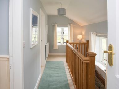 A hallway with a blue rug and a wooden railing overlooking a lower floor at Stabl Bach in Llanfaethlu