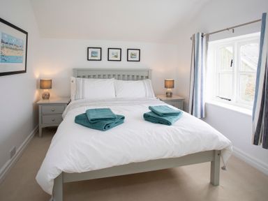 A bedroom with a bed two bedside tables lamps and a window with curtains at Stabl Bach in Llanfaethlu