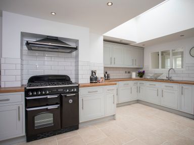 A kitchen with white cabinets a black stove a sink and a window at Stabl Bach in Llanfaethlu