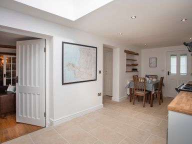 A kitchen with a dining table and chairs a map on the wall and an open door leading to a living room at Stabl Bach in Llanfaethlu