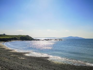 A coastal beach with pebbles and water reflecting sunlight at Stabl Bach in Llanfaethlu