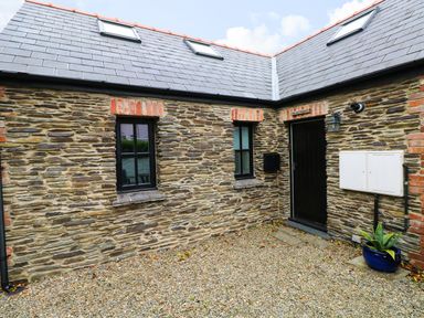 Stony courtyard with two small windows a black door and a potted plant at The Old Stables in Fishguard