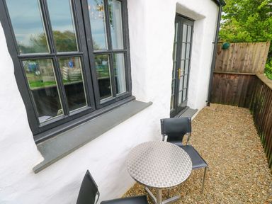 An outdoor patio area with a small round metal table and two black chairs beside white walls and black-framed windows at The Old Stables in Fishguard