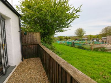 A fenced gravel patio area next to a white building with a garden and allotment plots in the background at The Old Stables in Fishguard
