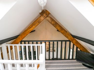 A loft area with wooden beams white and black railings striped carpet and a television at The Old Stables in Fishguard