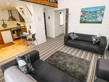 A living room with black sofas a small dining table and kitchenette at The Old Stables in Fishguard
