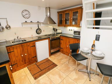 A kitchen with wooden cabinets a small dining table with two chairs and a clock on the wall at The Old Stables in Fishguard