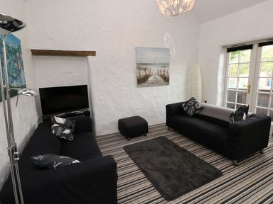 A living room with two black sofas a black ottoman a television and glass doors at The Old Stables in Fishguard