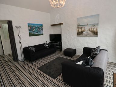 A living room with two black sofas a television and paintings on the wall at The Old Stables in Fishguard