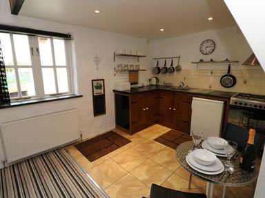 A kitchen with wooden cabinets and hanging pots next to a dining table with plates and glasses at The Old Stables in Fishguard