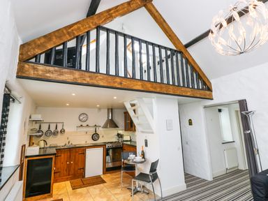 A kitchen area with wooden cabinets and hanging pans under a wood and black mezzanine at The Old Stables in Fishguard
