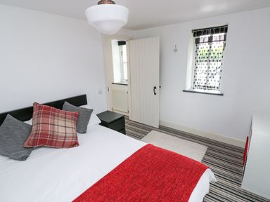 A bedroom with a bed with pillows and a red blanket a window with patterned blinds and a door at The Old Stables in Fishguard
