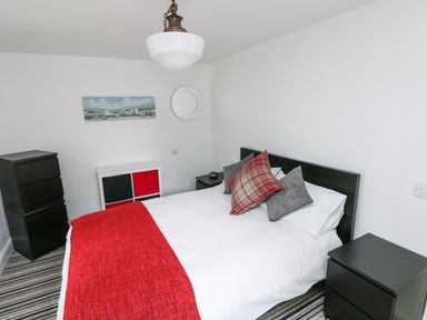 A bedroom with a bed with white bedding and red throw and pillows black bedside tables and dressers and a painting on the wall at The Old Stables in Fishguard