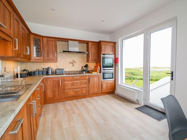 A kitchen with wooden cabinets and appliances next to a glass door overlooking green fields at Seacoast Cottage in Castlerock