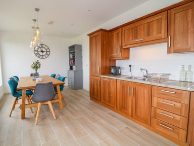 A kitchen with wooden cabinets a dining table with chairs a clock on the wall and a gray cabinet at Seacoast Cottage in Castlerock