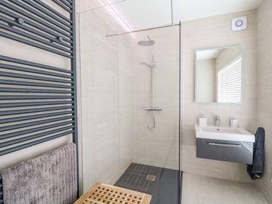 A bathroom with a shower area a wall-mounted sink mirror towel rack and a window with blinds at Seacoast Cottage in Castlerock