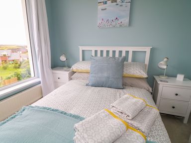 A bedroom with a bed pillows bedside tables lamps and a window at Seacoast Cottage in Castlerock